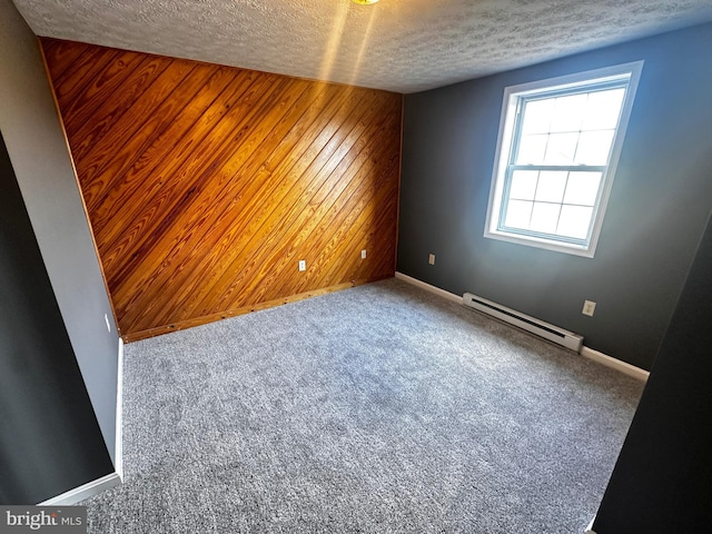 carpeted empty room featuring a textured ceiling, an accent wall, wood walls, and a baseboard radiator