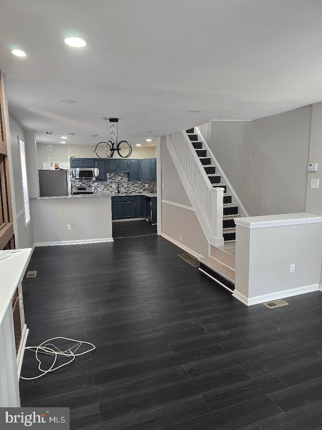 unfurnished living room with recessed lighting, dark wood-type flooring, an inviting chandelier, and stairs