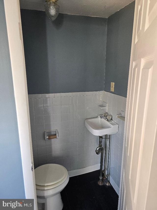 half bathroom with tile walls, toilet, a wainscoted wall, and a sink