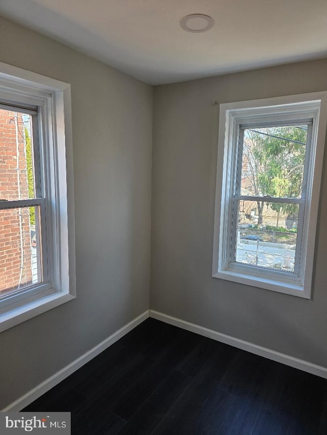 empty room featuring baseboards, plenty of natural light, and dark wood-style flooring