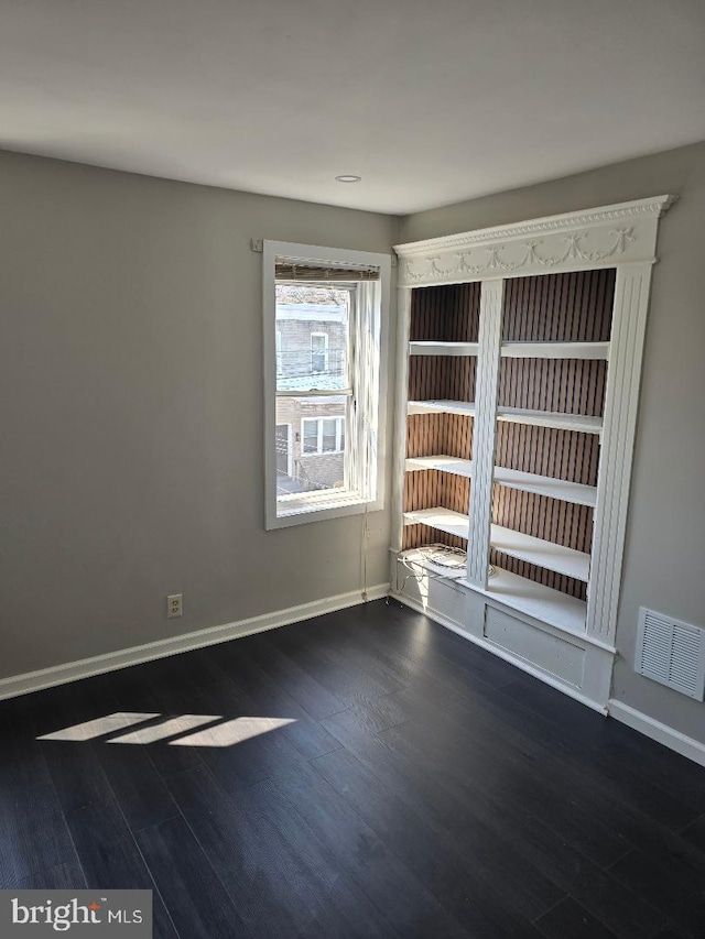 spare room featuring visible vents, baseboards, and dark wood-type flooring