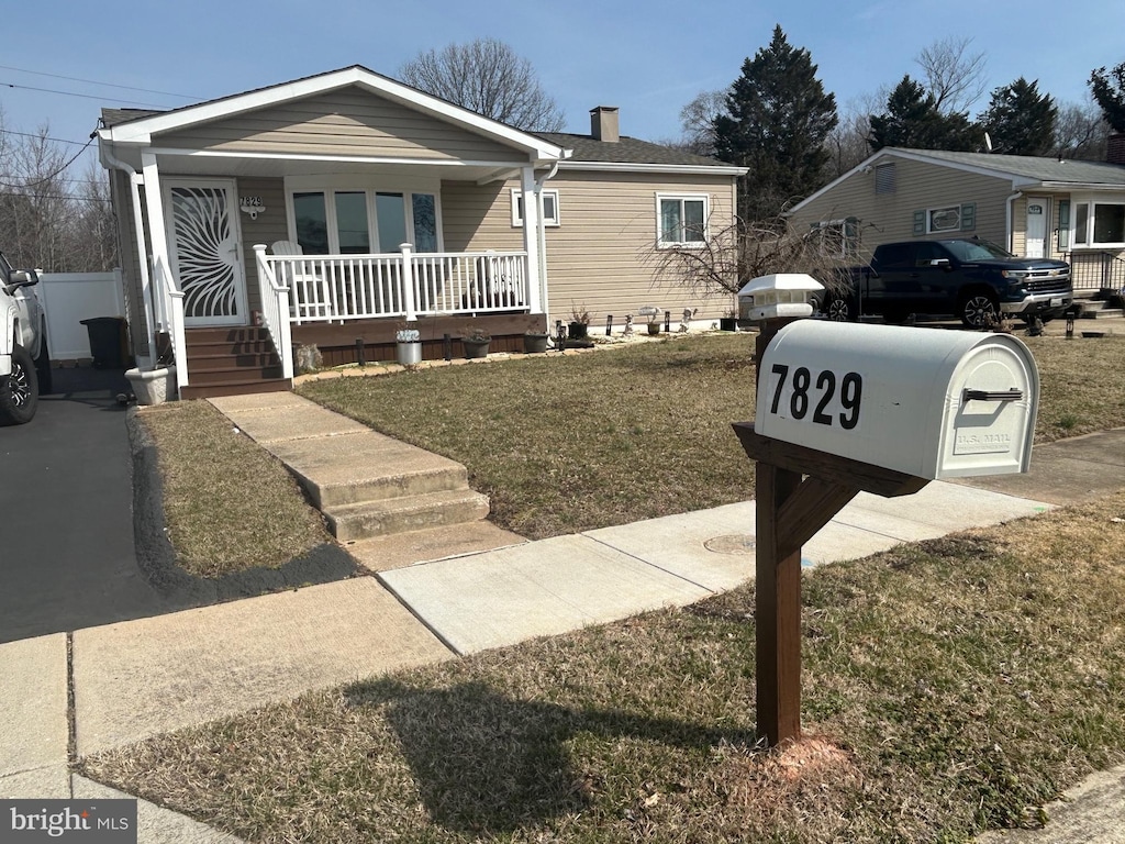 bungalow-style home with a porch, a chimney, and a front lawn