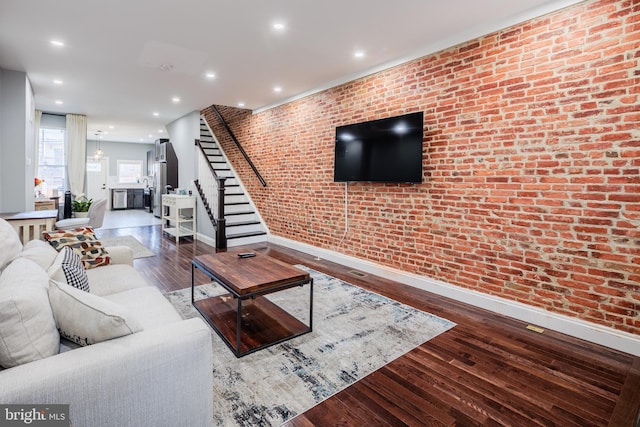 living room with stairs, recessed lighting, wood finished floors, and brick wall