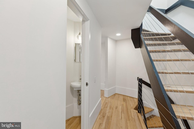 hall featuring baseboards, light wood-style floors, and an upstairs landing