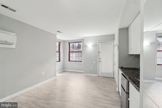 kitchen with dishwashing machine, a wall unit AC, visible vents, light wood-style flooring, and white cabinetry