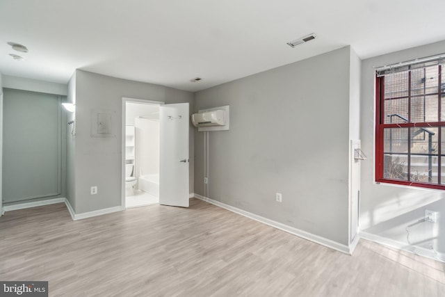 unfurnished bedroom featuring ensuite bath, light wood-style floors, visible vents, and baseboards