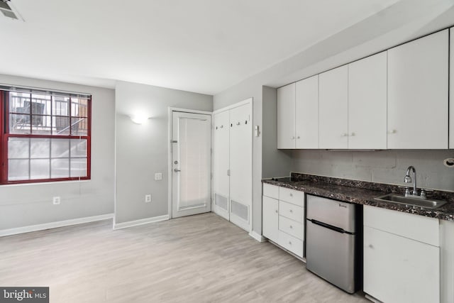 kitchen featuring dark stone counters, light wood-style flooring, freestanding refrigerator, white cabinets, and a sink