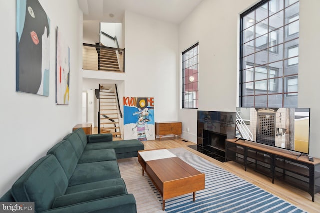 living room featuring a tiled fireplace, stairway, wood finished floors, and a high ceiling