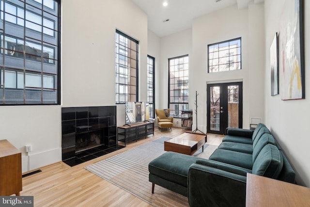 living room featuring wood finished floors, visible vents, baseboards, a towering ceiling, and a tiled fireplace