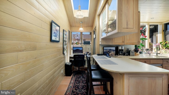 kitchen featuring light brown cabinets, light countertops, a peninsula, a kitchen breakfast bar, and a sink