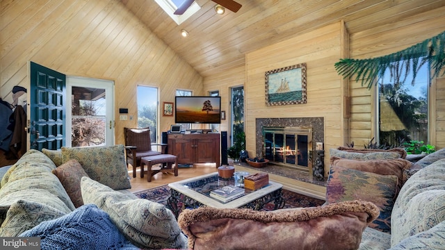 living area featuring ceiling fan, wooden walls, a skylight, and high vaulted ceiling