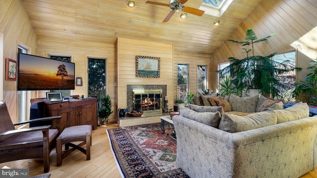 living room featuring a glass covered fireplace, vaulted ceiling with skylight, hardwood / wood-style floors, and ceiling fan