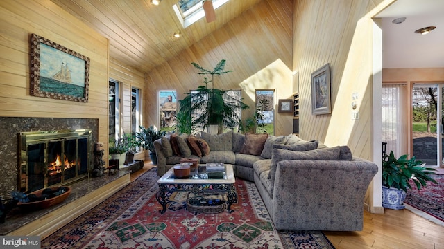 living room with wooden walls, high vaulted ceiling, a skylight, a fireplace, and hardwood / wood-style flooring