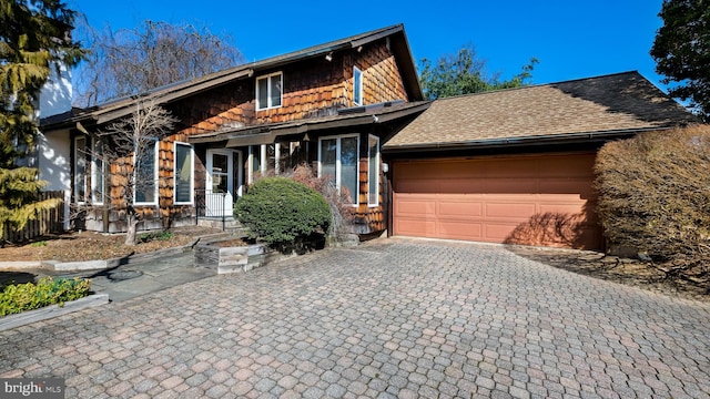 view of front of home with an attached garage, a shingled roof, and decorative driveway