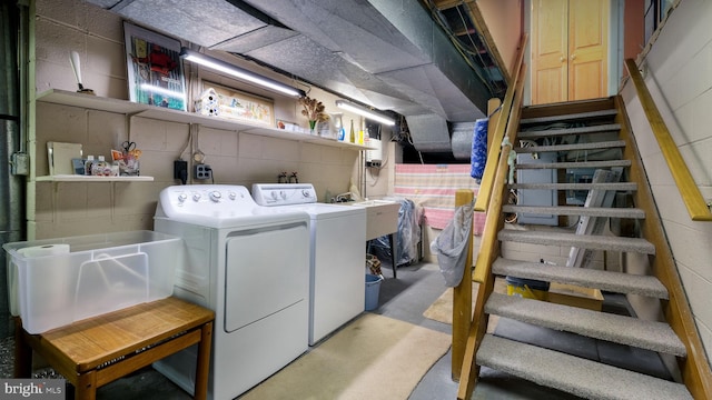 clothes washing area featuring a sink, concrete block wall, laundry area, and washing machine and clothes dryer