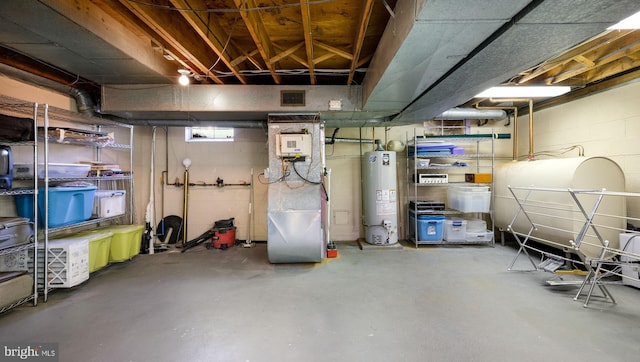 basement with gas water heater, visible vents, and concrete block wall