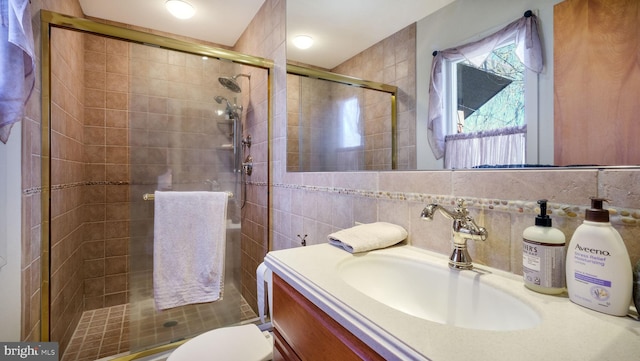 bathroom with vanity, a stall shower, tile walls, toilet, and tasteful backsplash