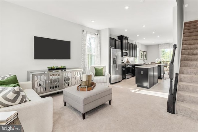 living room featuring light carpet, plenty of natural light, recessed lighting, and stairs