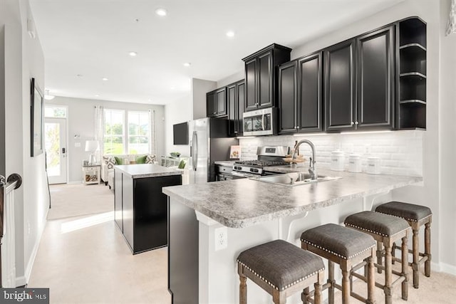 kitchen featuring dark cabinetry, a sink, stainless steel appliances, backsplash, and a center island