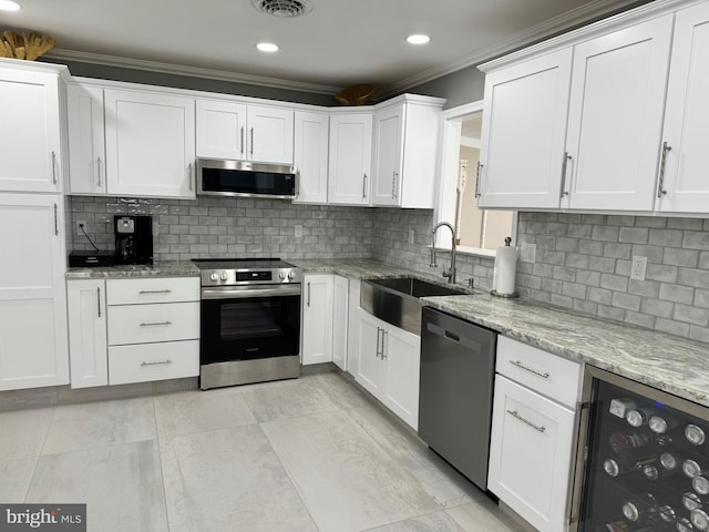 kitchen with a sink, wine cooler, appliances with stainless steel finishes, white cabinetry, and crown molding