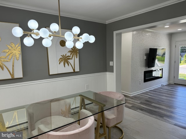 dining room with ornamental molding, wainscoting, a fireplace, wood finished floors, and a notable chandelier