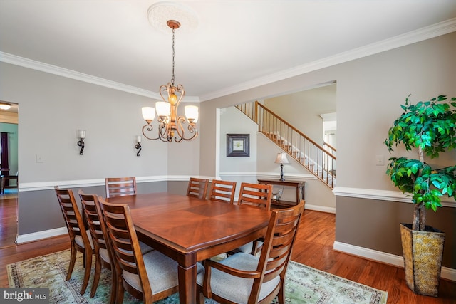 dining area featuring wood finished floors, crown molding, baseboards, a chandelier, and stairs