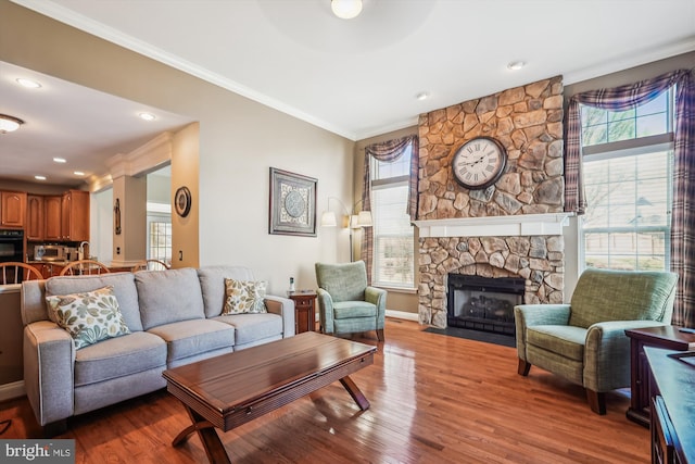 living room featuring plenty of natural light, wood finished floors, a stone fireplace, and ornamental molding