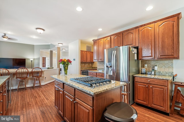 kitchen with light stone countertops, wood finished floors, wine cooler, appliances with stainless steel finishes, and a center island