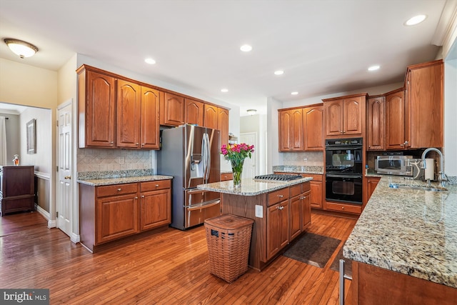 kitchen featuring light stone counters, brown cabinets, appliances with stainless steel finishes, hardwood / wood-style flooring, and a sink