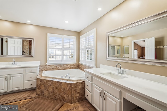 bathroom featuring a bath, recessed lighting, two vanities, and a sink