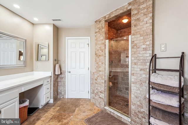 bathroom featuring vanity, visible vents, a stall shower, stone finish floor, and tile walls