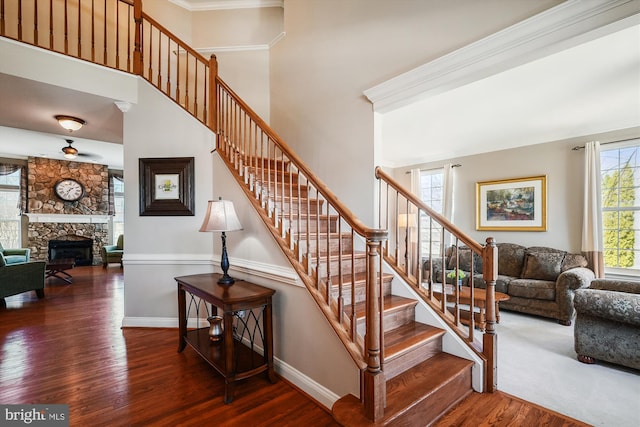 stairs with baseboards, a high ceiling, a stone fireplace, and wood finished floors