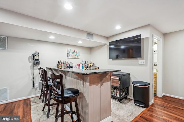 bar with light wood finished floors, visible vents, a dry bar, and baseboards