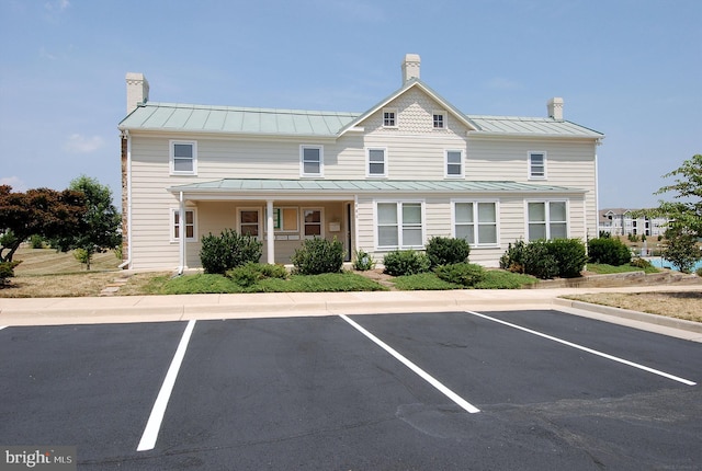 view of front of property with metal roof, uncovered parking, a chimney, and a standing seam roof