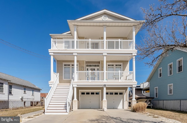 coastal home with concrete driveway, stairs, covered porch, a balcony, and an attached garage