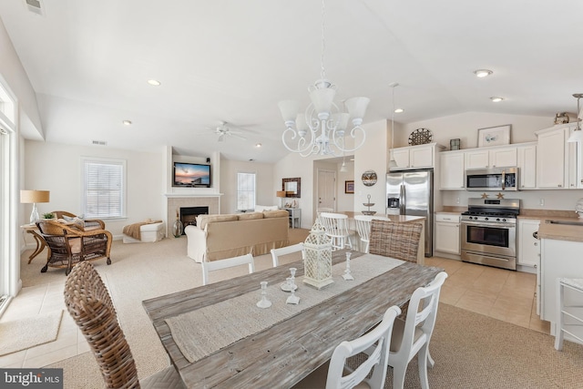 dining area featuring light carpet, a tiled fireplace, recessed lighting, light tile patterned floors, and vaulted ceiling