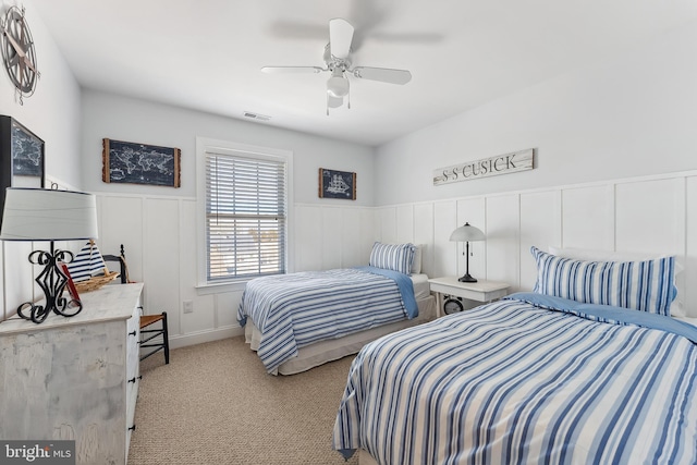 bedroom with visible vents, ceiling fan, a wainscoted wall, light carpet, and a decorative wall