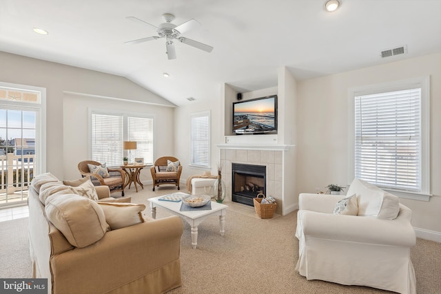 living area featuring a ceiling fan, visible vents, lofted ceiling, a tiled fireplace, and carpet flooring