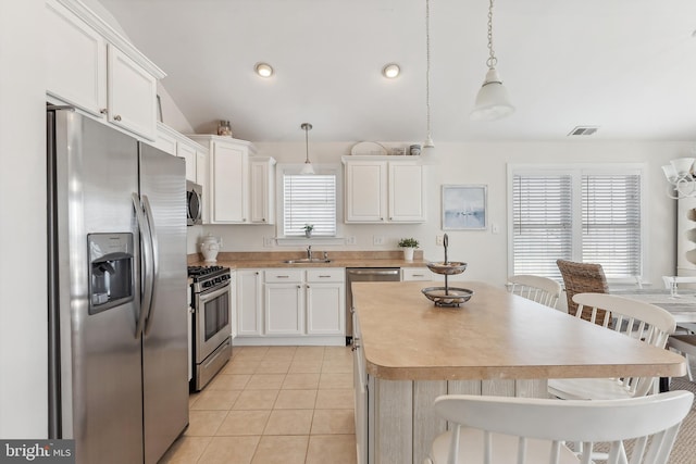 kitchen with a sink, a center island, stainless steel appliances, light tile patterned floors, and lofted ceiling