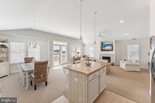 kitchen with a tiled fireplace, decorative light fixtures, lofted ceiling, light carpet, and ceiling fan with notable chandelier