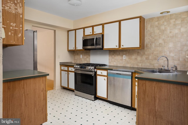 kitchen featuring dark countertops, backsplash, appliances with stainless steel finishes, and a sink