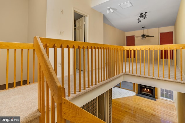 stairs with track lighting, a fireplace with flush hearth, wood finished floors, and ceiling fan