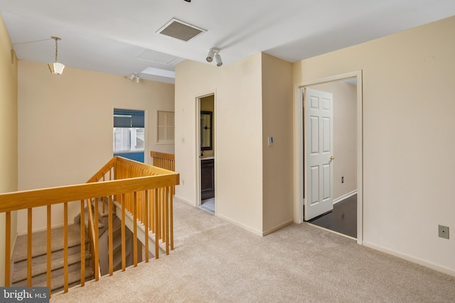 hallway with an upstairs landing, visible vents, light colored carpet, and baseboards