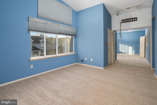 empty room with carpet, visible vents, baseboards, track lighting, and a towering ceiling