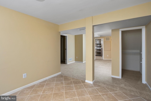 empty room featuring light carpet, visible vents, baseboards, and light tile patterned floors