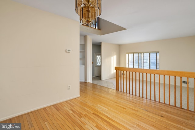 empty room with visible vents, wood-type flooring, a notable chandelier, and baseboards