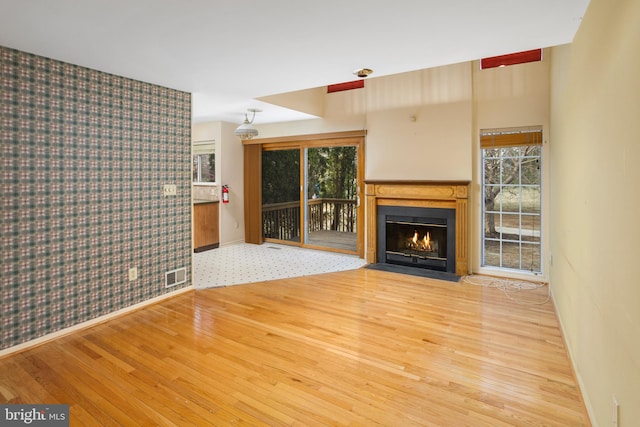 unfurnished living room with a wealth of natural light, visible vents, a fireplace with flush hearth, and wood finished floors