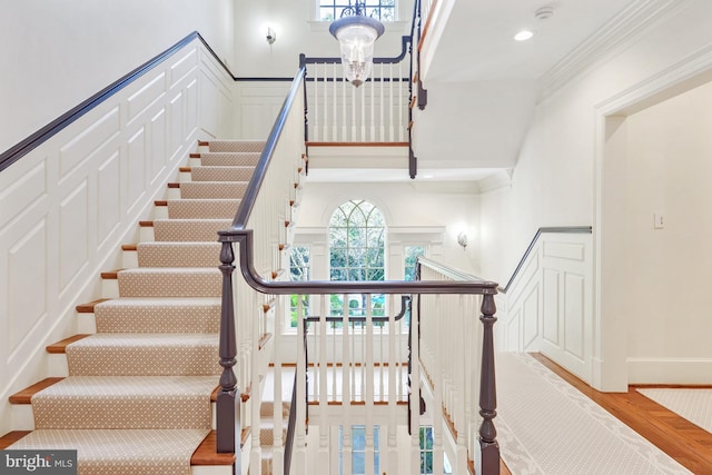 stairway with recessed lighting, a decorative wall, wainscoting, and crown molding