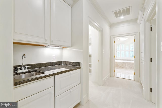 kitchen with visible vents, dark stone counters, ornamental molding, white cabinetry, and a sink