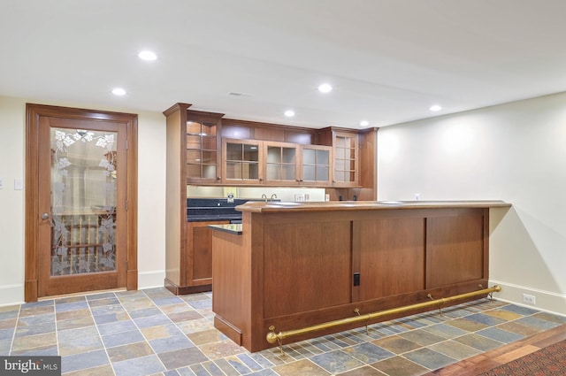 kitchen featuring recessed lighting, glass insert cabinets, brown cabinets, and baseboards